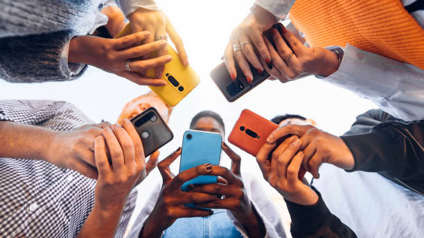 istockphoto-1371958166-612x612 Teens in circle holding smart mobile phones - Multicultural young people using cellphones outside - Teenagers addicted to new technology concept